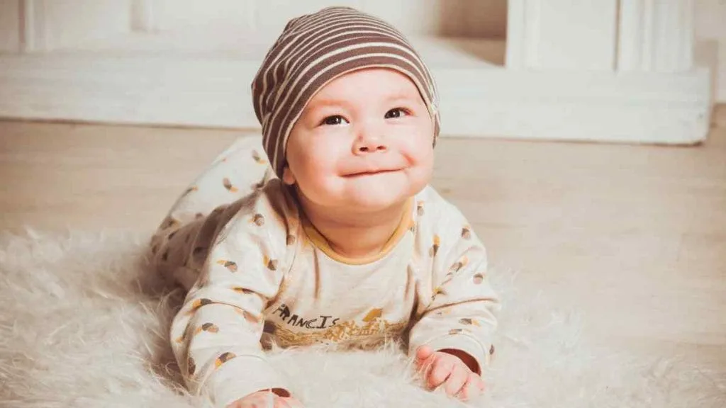 Bebê de gorro sorrindo, deitado sobre um tapete felpudo