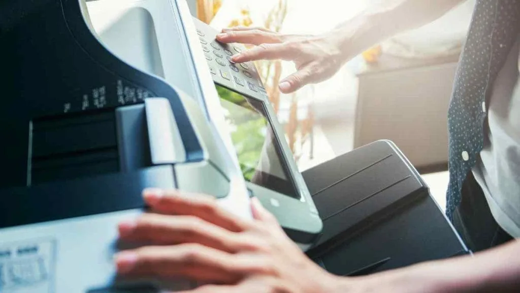 Mãos operando o painel de uma impressora multifuncional