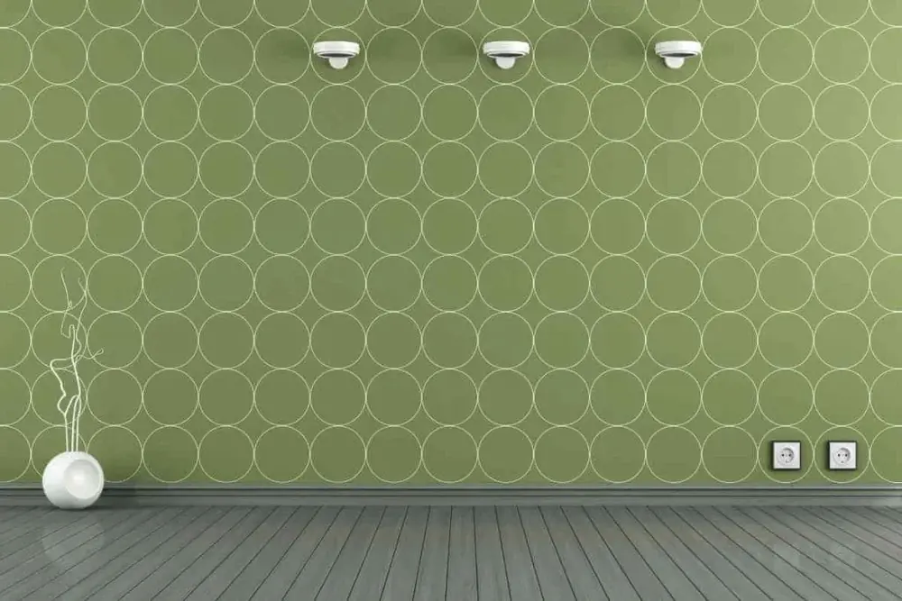 Parede verde com papel de parede estampado e um vaso branco no canto