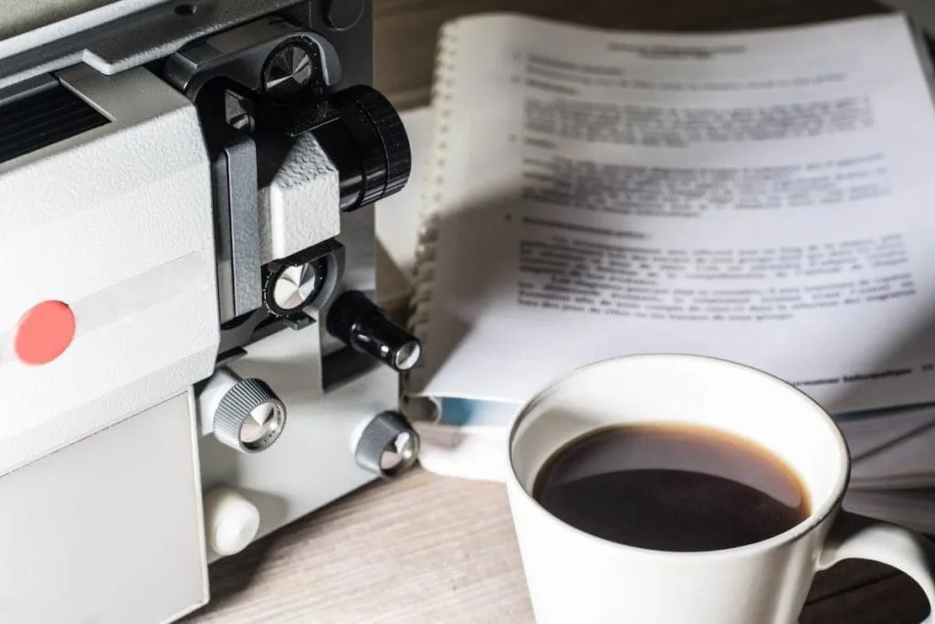 Projetor de cinema ao lado de uma xícara de café e folhas impressas